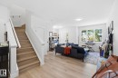 Open-concept living space featuring light wood-finish flooring, white walls, and a prominent staircase with white risers and wood treads - 11007 132 Street, Edmonton, AB 
