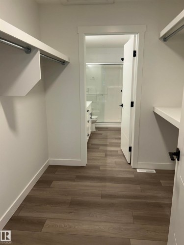 Walk-in closet featuring wood-finish flooring, white walls, and built-in shelving with hanging rods - 11007 132 Street, Edmonton, AB 