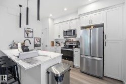 Modern kitchen featuring white shaker cabinetry, stainless steel appliances, a center island with a white countertop, and dark pendant lighting - 
