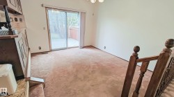 Spacious room featuring light-colored walls, patterned carpeting, and a sliding glass door providing access to an outdoor deck - 