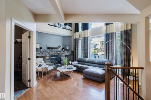 Spacious living area featuring high ceilings, wood-finish flooring, a stone-faced fireplace, and large windows with architectural detailing - 5206 Cercle Ciel Crescent, Beaumont, AB 