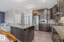 Gourmet kitchen featuring dark wood-finish cabinetry, stainless steel appliances, a large island with an undermount sink, and a multi-tone backsplash - 4105 171A Avenue, Edmonton, AB 