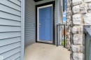 Entryway featuring a bold blue door, light gray siding, dark trim, stone facade, and black metal railing - 9328 Pear Link Link, Edmonton, AB 