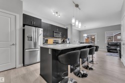 Open-concept kitchen featuring an island with seating, dark wood-finish cabinetry, stainless steel appliances, and light wood-finish flooring - 