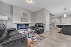 Living area featuring light wood-finish flooring, a contemporary fireplace with a stone surround, and a white mantel - 