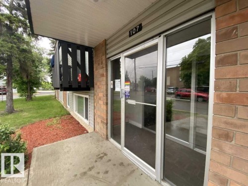 Brick exterior featuring large glass entrance doors and a concrete walkway - 107 Village Acres Northwest, Edmonton, AB - Outdoor With Exterior