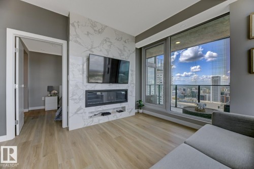 Contemporary living area featuring wide plank wood-finish flooring and a full-height window wall with cityscape scenery - 2902 10180 103 Street, Edmonton, AB 