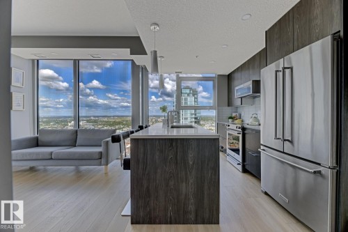 Modern kitchen featuring an island with a light-toned countertop, stainless steel appliances, dark wood-finish cabinetry, and light wood-finish flooring - 2902 10180 103 Street, Edmonton, AB 