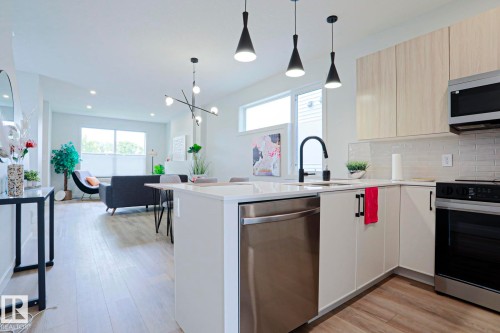 Open-concept kitchen featuring an island with pendant lighting, stainless steel appliances, light wood-finish flooring, white cabinetry, and a subway tile backsplash - 12842 121 Street, Edmonton, AB 