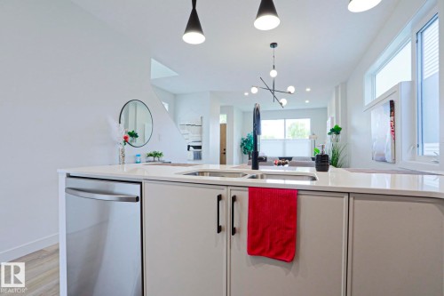 Kitchen island featuring a stainless steel undermount sink with a black gooseneck faucet, light-toned cabinetry, and a stainless steel dishwasher - 12842 121 Street, Edmonton, AB 