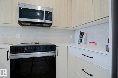 Kitchen featuring a built-in stainless steel microwave, light wood-finish upper cabinetry, white subway tile backsplash, white countertops, and black hardware - 12842 121 Street, Edmonton, AB 