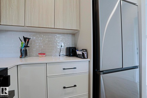 Kitchen featuring light wood-finish upper cabinetry and white lower cabinetry with matte black hardware - 12842 121 Street, Edmonton, AB 