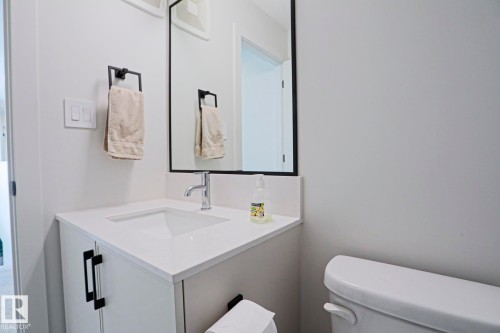 White vanity with a built-in rectangular sink, light-toned countertop, chrome faucet, and matte black hardware - 12842 121 Street, Edmonton, AB 