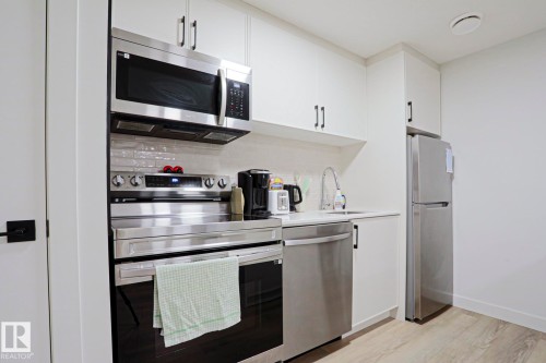 Modern kitchen featuring white cabinetry, stainless steel appliances, a subway tile backsplash, light-toned wood-finish flooring, and a built-in microwave - 12842 121 Street, Edmonton, AB 