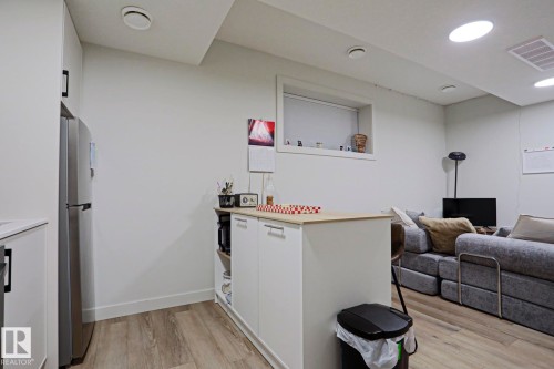 Open-concept living area featuring wood-finish flooring, recessed lighting, a stainless steel refrigerator, and a kitchen island with light wood-finish countertop - 12842 121 Street, Edmonton, AB 