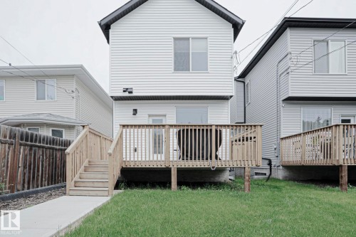 Rear exterior featuring a spacious wood deck with railings and stairs, a grass lawn, and a concrete pathway - 12842 121 Street, Edmonton, AB 