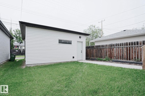 Detached garage featuring white horizontal siding, a flat roofline with black trim, and a side entry door - 12842 121 Street, Edmonton, AB 