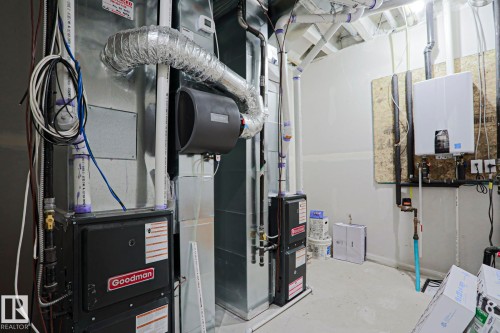 Dedicated utility room featuring a Goodman furnace, various ductwork, and a wall-mounted tankless water heater - 12842 121 Street, Edmonton, AB 