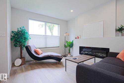 Living area featuring a modern linear fireplace, light wood-finish flooring, recessed lighting, a large window, and light wall tones - 12842 121 Street, Edmonton, AB 