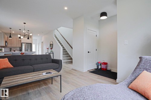 Open-concept living area featuring light wood-finish flooring, recessed lighting, a modern kitchen with light wood-tone cabinetry, and a stainless steel refrigerator - 12842 121 Street, Edmonton, AB 