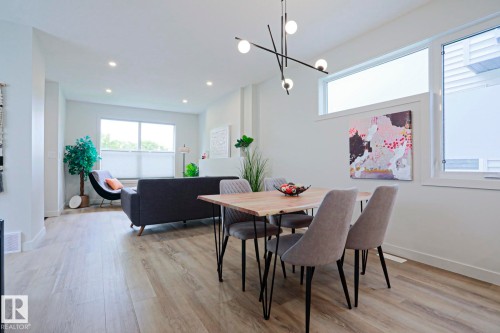 Dining area featuring a contemporary linear chandelier with spherical lights, wood-finish flooring, and white baseboards - 12842 121 Street, Edmonton, AB 