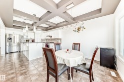 Open-concept kitchen featuring a coffered ceiling, white cabinetry, stainless steel appliances, a center island with pendant lighting, and tile flooring - 