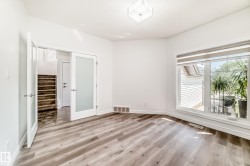 Spacious room featuring wood-finish flooring, a large window with blinds, and white trim - 