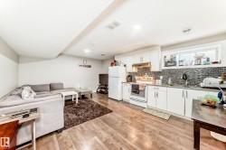 Open-concept living space featuring wood-finish flooring, recessed lighting, and a white kitchen with a mosaic tile backsplash - 