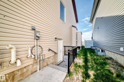 Cream-colored vinyl siding exterior with a concrete pathway leading to a white entry door, featuring a black metal railing - 