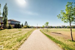 Paved pathway bordered by extensive grassy areas and mature trees, with residential properties visible in the background - 