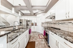 Contemporary kitchen featuring white cabinetry, dark stone countertops, stainless steel appliances, and a tiled backsplash - 