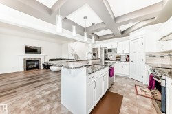 Open-concept kitchen featuring an oversized island with an undermount sink, granite countertops, stainless steel appliances, and white cabinetry - 
