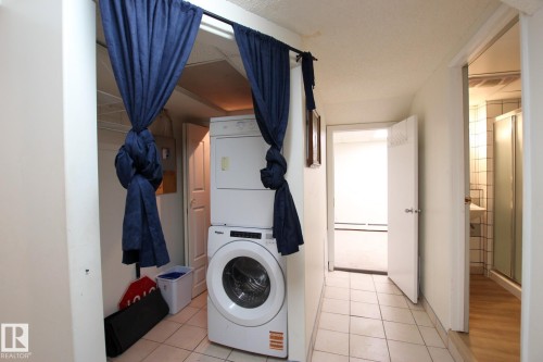 Laundry area featuring a stacked washer and dryer, tile flooring, and direct access to an additional room - 11242 56 Street, Edmonton, AB 