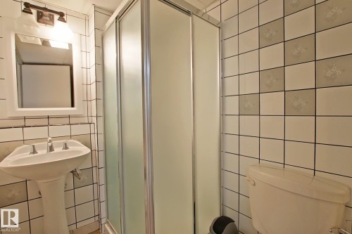 Bathroom with a pedestal sink, white subway tile, patterned accent tiles, a shower enclosure with frosted glass, and a toilet - 11242 56 Street, Edmonton, AB 