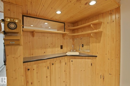 Custom wet bar area featuring extensive knotty pine paneling, recessed lighting, integrated sink with chrome faucet, corner shelving, and a mirrored backsplash - 11242 56 Street, Edmonton, AB 