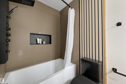 Modern bathroom featuring a soaking tub, matte black shower panel with multiple spray functions, recessed shower niche, contemporary wall paneling, and a black toilet - 12611 47 Street, Edmonton, AB 