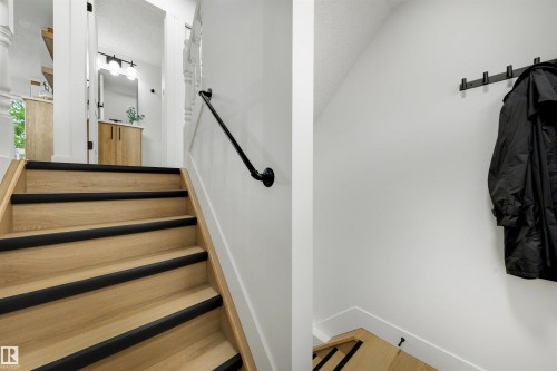 Staircase featuring light wood-finish treads with dark risers and a black handrail - 12611 47 Street, Edmonton, AB 