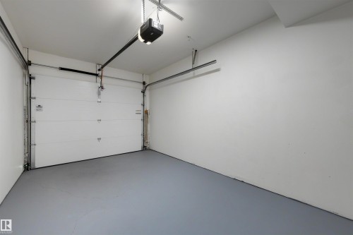 Spacious garage featuring a white overhead door, gray floor coating, white walls, and an overhead lighting fixture - 12611 47 Street, Edmonton, AB 