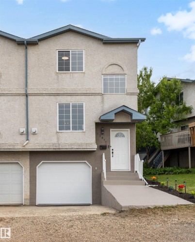 Three-story stucco exterior featuring a prominent arched window, white entry door with frosted glass, and an attached garage with a modern white door - 12611 47 Street, Edmonton, AB 