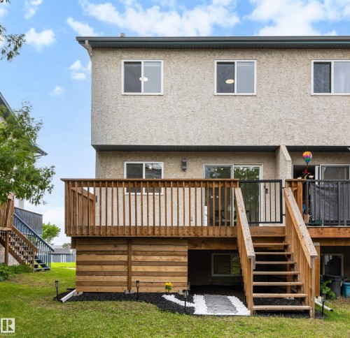 Rear exterior featuring a spacious wood deck with stairs to the yard, a stucco facade, and multiple windows - 12611 47 Street, Edmonton, AB 