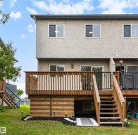 Rear exterior featuring a spacious wood deck with stairs to the yard, a stucco facade, and multiple windows - 