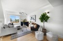 Bright living area featuring wood-finish flooring, a large window, a fireplace with a dark surround, track lighting, and a wall-mounted fixture - 12611 47 Street, Edmonton, AB 