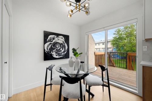 Bright dining area featuring light wood-finish flooring, a modern chandelier with spherical glass shades, and a sliding glass door providing direct access to an outdoor wooden deck with black metal railings - 12611 47 Street, Edmonton, AB 