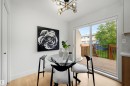 Bright dining area featuring light wood-finish flooring, a modern chandelier with spherical glass shades, and a sliding glass door providing direct access to an outdoor wooden deck with black metal railings - 12611 47 Street, Edmonton, AB 