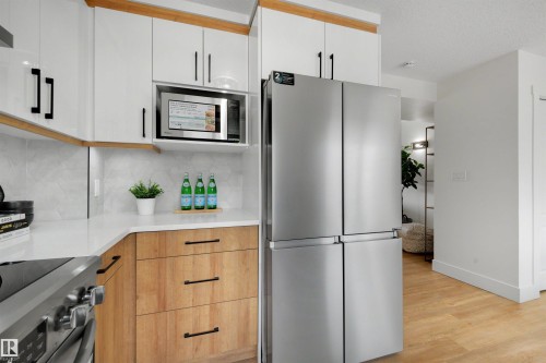 Contemporary kitchen featuring white upper cabinetry, wood-finish lower cabinetry, and light-toned countertops - 12611 47 Street, Edmonton, AB 