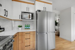 Contemporary kitchen featuring white upper cabinetry, wood-finish lower cabinetry, and light-toned countertops - 