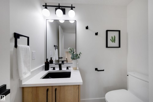 Modern bathroom vanity featuring a light wood-finish cabinet with black hardware, a light-toned countertop, and a black rectangular undermount sink - 12611 47 Street, Edmonton, AB 