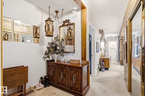 Entryway featuring a decorative wood-finish cabinet with detailed carvings, an ornate gold-framed mirror, and two hanging lantern-style light fixtures - 9747 67 Avenue, Edmonton, AB 