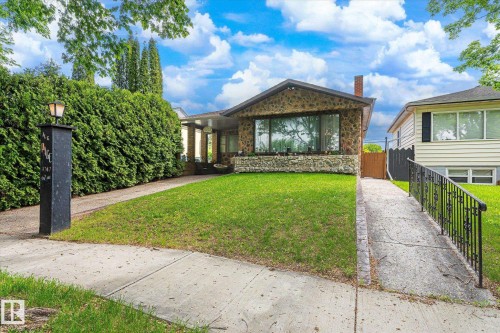 Stone facade residence featuring a prominent picture window, a covered entryway with pillars, and a red brick chimney - 9747 67 Avenue, Edmonton, AB 
