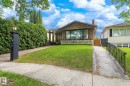 Stone facade residence featuring a prominent picture window, a covered entryway with pillars, and a red brick chimney - 9747 67 Avenue, Edmonton, AB 
